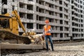 a great worker in uniform and helmet stands by an excavator on a construction site. Royalty Free Stock Photo