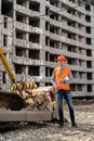 a great worker in uniform and helmet stands by an excavator on a construction site. Royalty Free Stock Photo