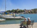 Greece, corfu, Kassiopi september 28, 2018: Two senior people couple tourist sitting on bench on Quay with view on
