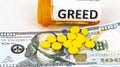 Greed written on pill bottle with money and yellow pills Royalty Free Stock Photo