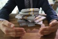 Greedy man in suit closes dollars pile with hands at desk Royalty Free Stock Photo