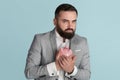 Greedy young businessman hugging piggy bank against blue background