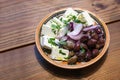 Greek appetizer snacks, herb olives, onions and feta cheese in a ceramic bowl on a rustic wooden table, copy space, selected focus