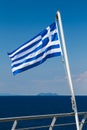 Greek flag on the blue sky and blue sea background at the aft of a ferry boat. Vertical. Royalty Free Stock Photo