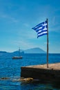 Greek flag in the blue sky on pier and traditional greek fishing boat in the Aegean sea Royalty Free Stock Photo