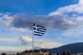 Greek flag flying against dramatic sky on Acropolis with tourists standing around it Athens Greece 01 03 2018 Royalty Free Stock Photo