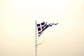 Greek flag torn by the storm, blowing in the wind. On a flagpole with a cross. Taken during the sunset. Royalty Free Stock Photo