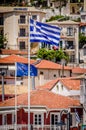 Greek Flag Waving Over Picturesque Coastal Town of Parga, Greece. European Union Flag and Traditional House Rooftops Royalty Free Stock Photo
