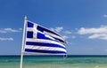 Greek flag waving in wind in blue sky and white clouds and sea waves around Royalty Free Stock Photo