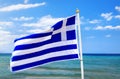 Greek flag waving in wind in blue sky and white clouds and sea waves around Royalty Free Stock Photo