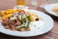 Greek Gyros meal from roasted sliced meat with French fries, onions, coleslaw and tzatziki on a white plate in an outdoor Royalty Free Stock Photo