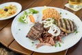 Greek mixed grill with grilled liver, Bifteki, Gyros, onions, tsatsiki, coleslaw and rice on wooden table
