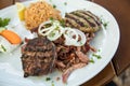 Greek mixed grill with grilled liver, Bifteki, Gyros, onions, Tsatsiki and rice on wooden table