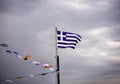 Greek national flag on flagpole and some other small flags waving against a dramatic blue sky Royalty Free Stock Photo