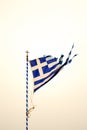 Greek national flag torn by the storm, blowing in the wind. On a flagpole with a cross. Taken during the sunset. Royalty Free Stock Photo