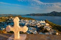 Christian cross and Plaka village on Milos island over red geranium flowers on sunset in Greece Royalty Free Stock Photo