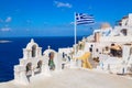 Greek orthodox church with bells and greek flag against famous white houses on Santorini island, Aegean sea, Greece Royalty Free Stock Photo