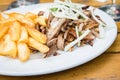 Greek pork meat Gyros with onions, Tsatsiki and French fries on wooden table in restaurant