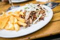Greek pork meat Gyros with onions, Tsatsiki and French fries on wooden table in restaurant