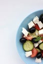 Greek salad in blue bowl on white background. Close-up of vegetable salad with fets cheese, black olives, cucumber and tomatoes. Royalty Free Stock Photo