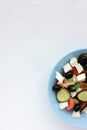 Greek salad in blue bowl on white background. Close-up of vegetable salad with fets cheese, black olives, cucumber and tomatoes. Royalty Free Stock Photo