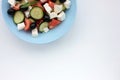 Greek salad in blue bowl on white background. Close-up of vegetable salad with fets cheese, black olives, cucumber and tomatoes. Royalty Free Stock Photo