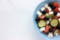 Greek salad in blue bowl on white background. Close-up of vegetable salad with fets cheese, black olives, cucumber and tomatoes. Royalty Free Stock Photo