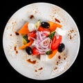 Greek salad in a bowl with fresh vegetables and feta cheese, isolated on black background. Top view Royalty Free Stock Photo