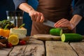 Greek salad. The chef cuts a cucumber on a cutting board. Feta cheese, lemon, cherry tomatoes are on the table. Rough wooden table Royalty Free Stock Photo