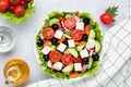Greek salad with feta cheese, cherry tomatoes, cucumbers, olives and seasoned with oil. White checkered napkin on gray table. Top Royalty Free Stock Photo