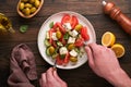 Greek salad. Fresh Greek salad with fresh vegetables, tomato, cucumber, green olives, feta cheese and man hands on old dark wooden Royalty Free Stock Photo