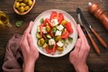 Greek salad. Fresh Greek salad with fresh vegetables, tomato, cucumber, green olives, feta cheese and man hands on old dark wooden Royalty Free Stock Photo