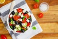 Greek salad of fresh juicy vegetables, feta cheese, herbs and olives in a white bowl on a wooden background. Healthy food. Royalty Free Stock Photo