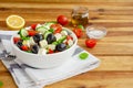 Greek salad of fresh juicy vegetables, feta cheese, herbs and olives in a white bowl on a wooden background. Healthy food. Royalty Free Stock Photo