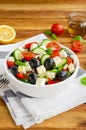 Greek salad of fresh juicy vegetables, feta cheese, herbs and olives in a white bowl on a wooden background. Healthy food. Royalty Free Stock Photo