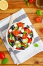 Greek salad of fresh juicy vegetables, feta cheese, herbs and olives in a white bowl on a wooden background. Healthy food. Royalty Free Stock Photo