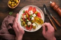 Greek salad. Fresh Greek salad with fresh vegetables, tomato, cucumber, green olives, feta cheese and man hands on old dark wooden Royalty Free Stock Photo