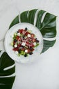 Greek salad with monstera leaf under plate, marble background