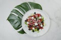 Greek salad with monstera leaf under plate, marble background