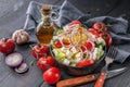 Greek salad with olive oil and spices. Onion, garlic, fork and spoon, gray napkin on a dark wooden table. Horizontal shot