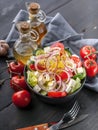 Greek salad with olive oil and spices. Onion, garlic, fork and spoon, gray napkin on a dark wooden table. Vertical shot