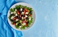 Greek salad on white plate on bright blue table, top view, copy space Royalty Free Stock Photo