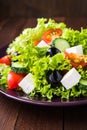 Greek salad (lettuce, tomatoes, feta cheese, cucumbers, black olives) on dark wooden background close up Royalty Free Stock Photo