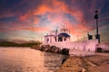 Greek small chapel with white roofs on cliff over sea and small bay under a dramatic sky at sunset Royalty Free Stock Photo