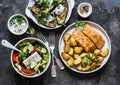 Greek style lunch table - baked lemon salmon with potatoes, greek salad, grilled eggplant with tzadziki sauce on dark background,