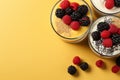 Yogurt and berry bowls with spoon and towel on bright white and yellow background, space for text
