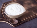 Greek yogurt in a gray oval clay bowl and wooden spoon on wooden chopping board. Royalty Free Stock Photo