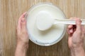 Greek yogurt in kitchen spoon in woman hand took it from glass bowl on wooden background