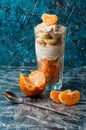 Greek yogurt with tangerine, banana and oatmeal in a tall glass, a vintage spoon and slices of citrus on the table