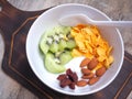 Greek yogurt in a white bowl topped with kiwi, almonds, dried strawberries, and cornflakes, on a wooden cutting board.